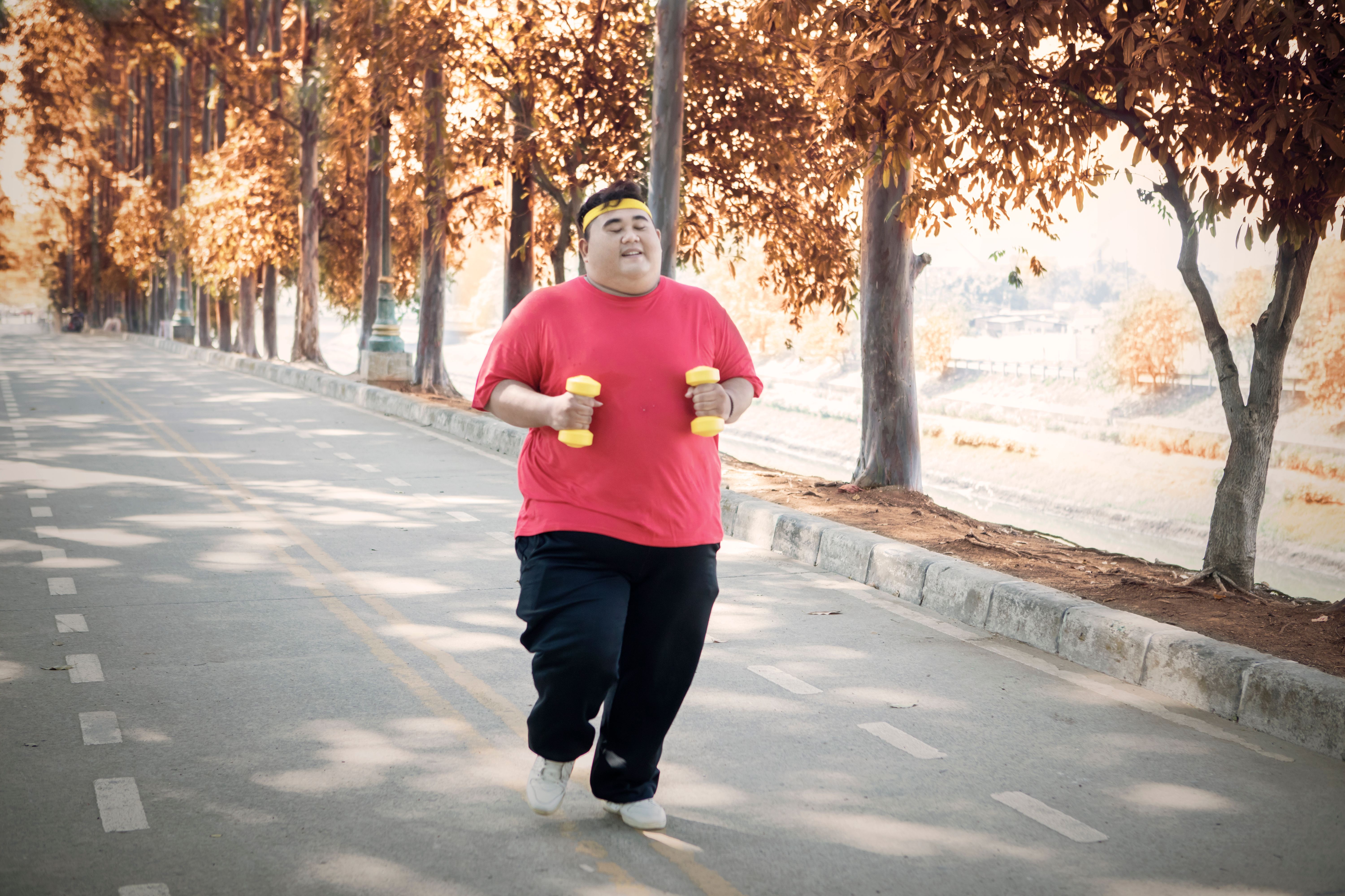 overweight-man-holding-dumbbells-while-running-road-park.jpg